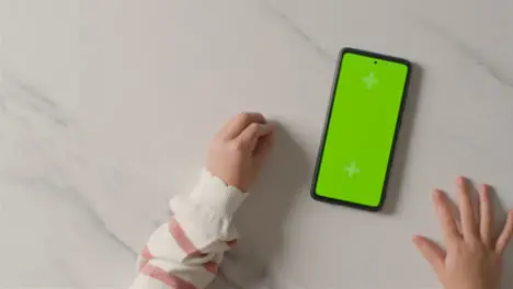 Overhead Studio Shot Of Child Scrolling On Green Screen Mobile Phone