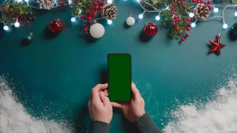 Overhead Shot Of Person Holding Green Screen Mobile Phone Above Christmas Decorations