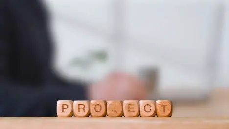 Business Concept Wooden Letter Cubes Or Dice Spelling Project With Office Person Using Mobile Phone In Background