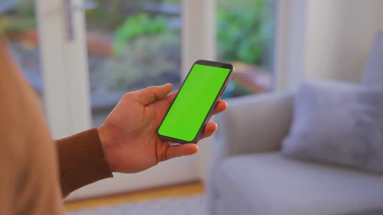 Close Up Of Man At Home Holding Phone With Blank Green Screen