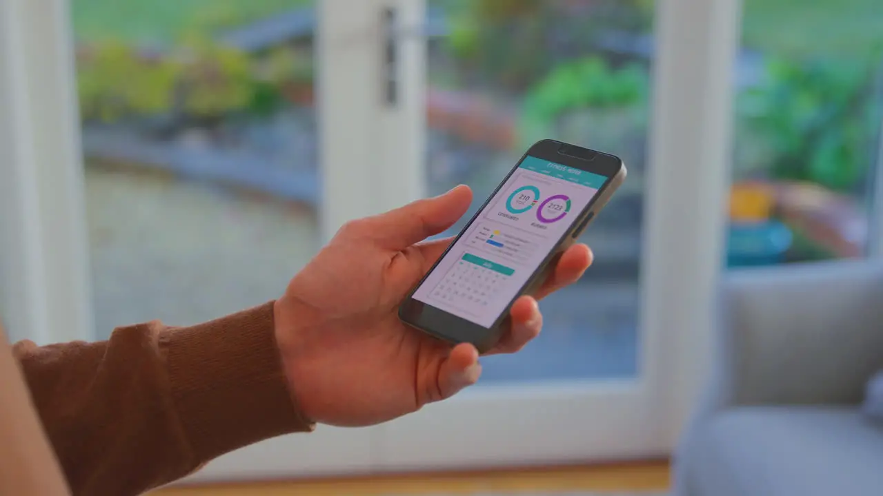 Close Up Of Man At Home Holding Phone Looking At Fitness Tracker App