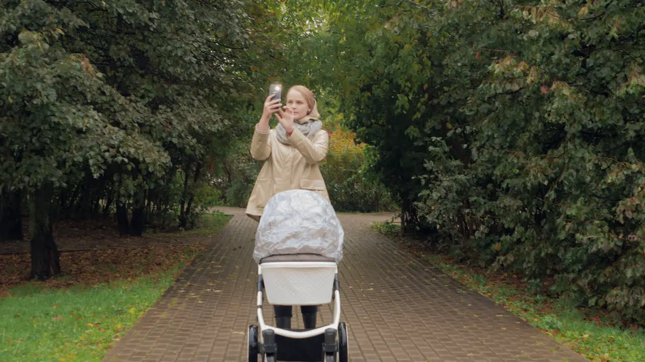 A woman with a baby carriage in a park taking pictures