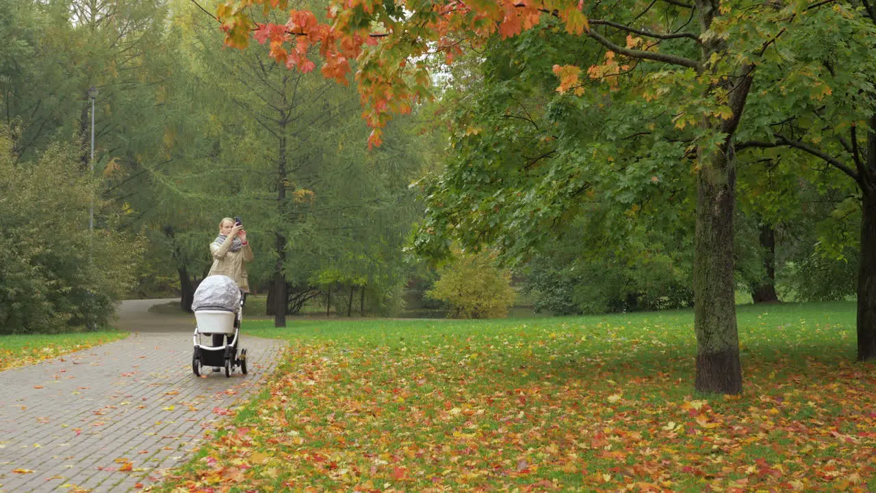 A woman walking with a baby carriage in an autumn park