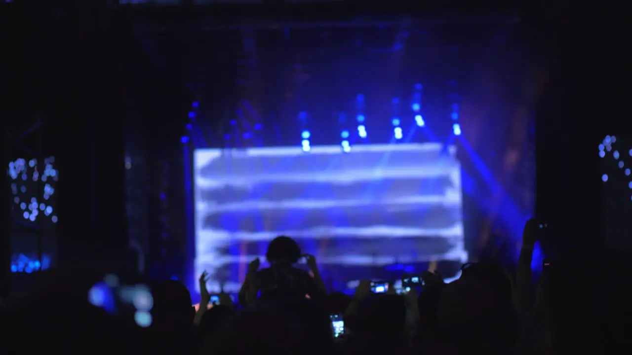 A slow motion of a crowd in front of the bright stage at an open air concert