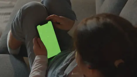 Young Girl At Home Relaxing On Sofa Looking At Green Screen Mobile Phone