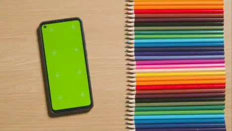 Coloured Pencils In A Line On Wooden Background With Person Scrolling On Green Screen Mobile Phone 1