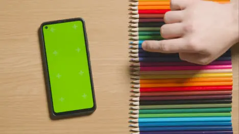 Coloured Pencils In A Line On Wooden Background With Person Choosing Purple One And Green Screen Mobile Phone