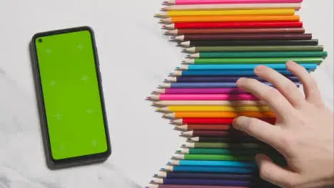 Coloured Pencils In A Line On Marble Background With Person Choosing Red One And Green Screen Mobile Phone 1