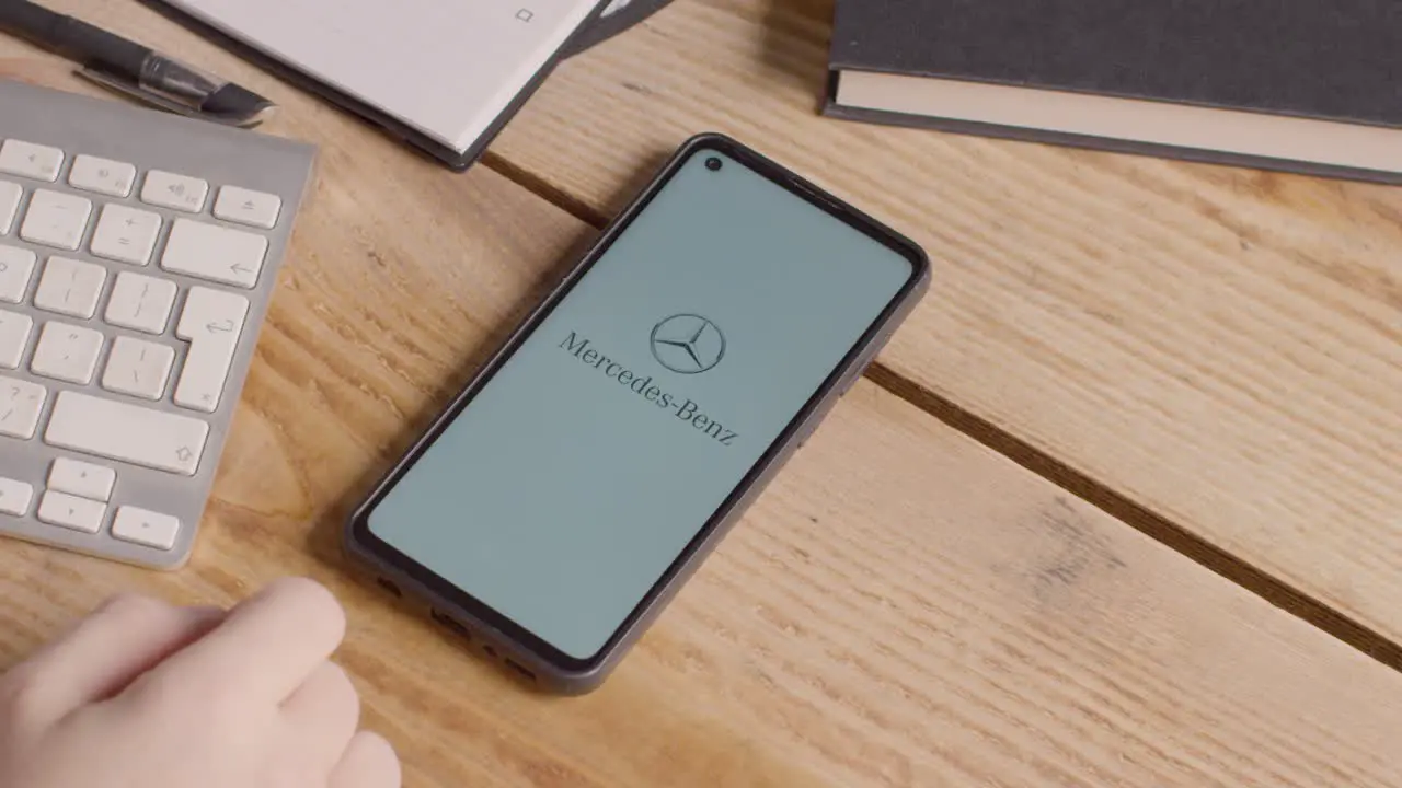 Mobile Phone On Desk With Screen Showing Brand Logos For Tesla Mercedes Benz BMW and Toyota