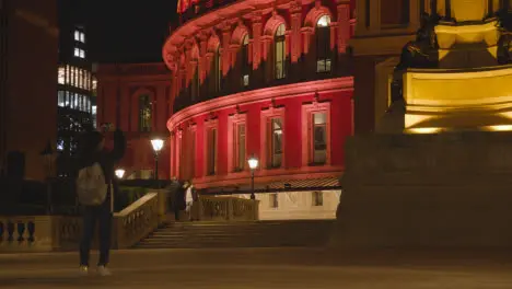 Person With Phone Taking Picture Of Exterior Of The Royal Albert Hall in London UK Floodlit At Night