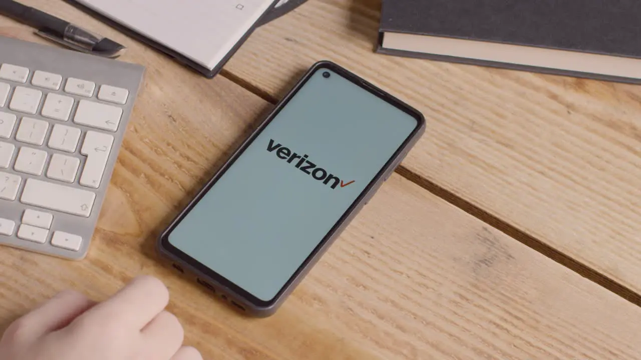 Mobile Phone On Desk With Screen Showing Brand Logos For Tencent Verizon AT&T Spectrum Xfinity and Apple