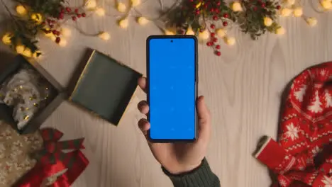 Overhead Shot Of Person Holding Blue Screen Mobile Phone With Christmas Decorations And Wrapping