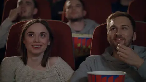 Young people enjoying film in cinema Couple eating popcorn and watching movie