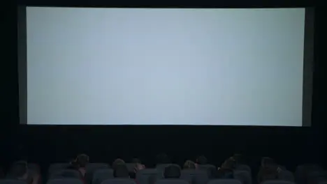 Spectators applaud in anticipation of movie session in front of white screen