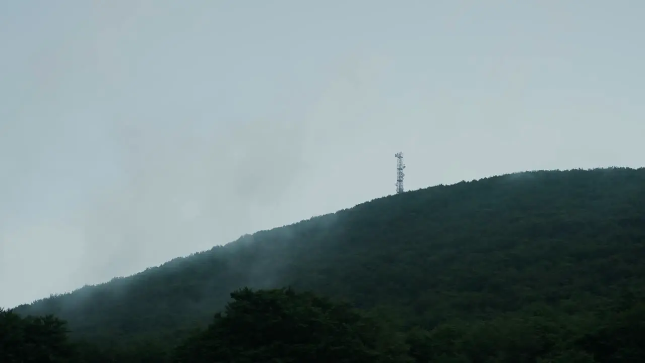 An antenna is seen on top of a mountain during a cloudy day