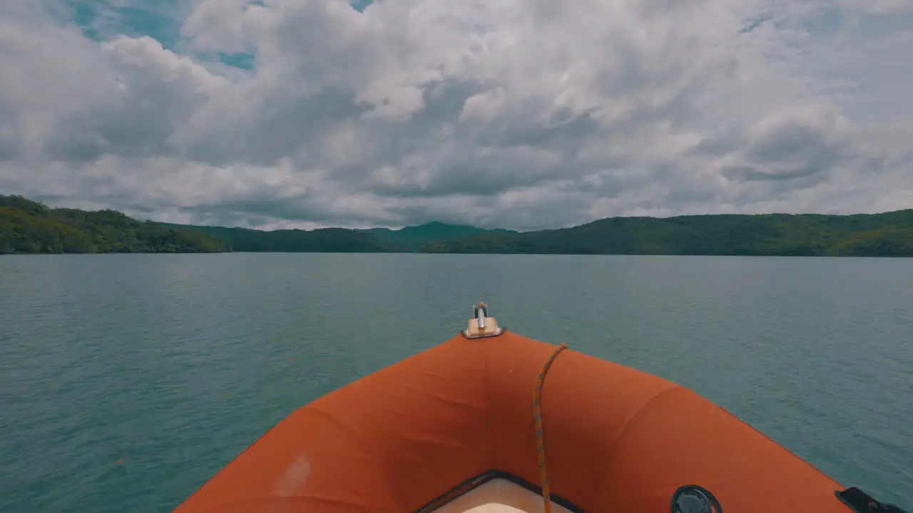 View from the front of an orange speed boat driving fast in the sea with coasts of some island in the background during a cloudy day