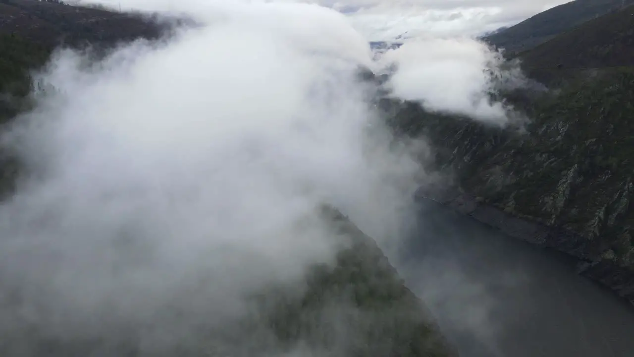 Flying through clouds over a lake forest and mountains in Spain