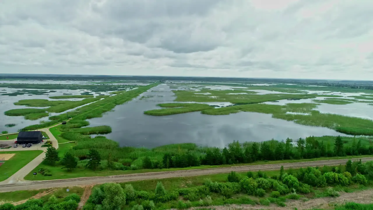 Aerial of lake in rural landscape on cloudy day near farm and green grass Europe