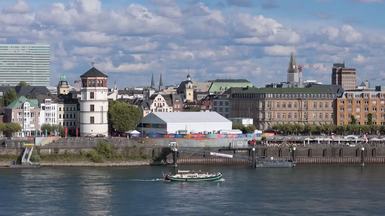 A small riverboat passes by Düsseldorf on the Rhine under a cloudy sky