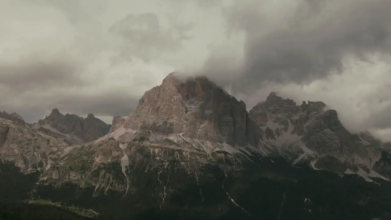 Aerial view with distant steep tall mountains touching the clouds green forest at the bottom Alps rocky mountains before storm rainy day cinematic grade