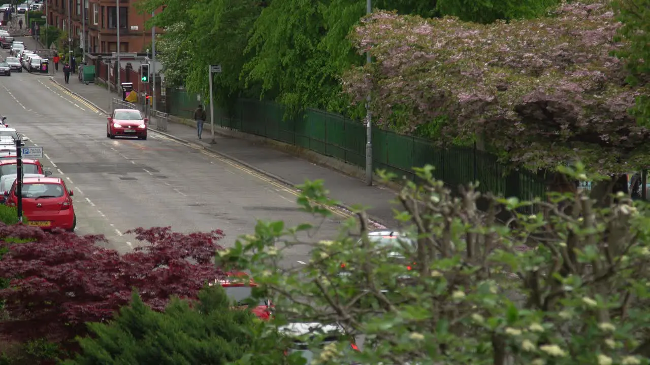 Long shot down street of a cloudy winter day in Glasgow West End with vegetation and cars