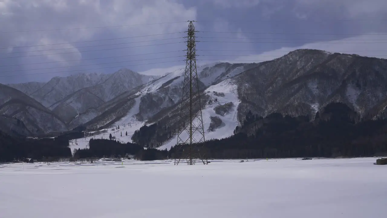 Against the dramatic winter landscape of Hakuba Japan a captivating shot reveals an electrical pylon amidst the cloudy skies as two cars elegantly traverse the snow-covered terrain