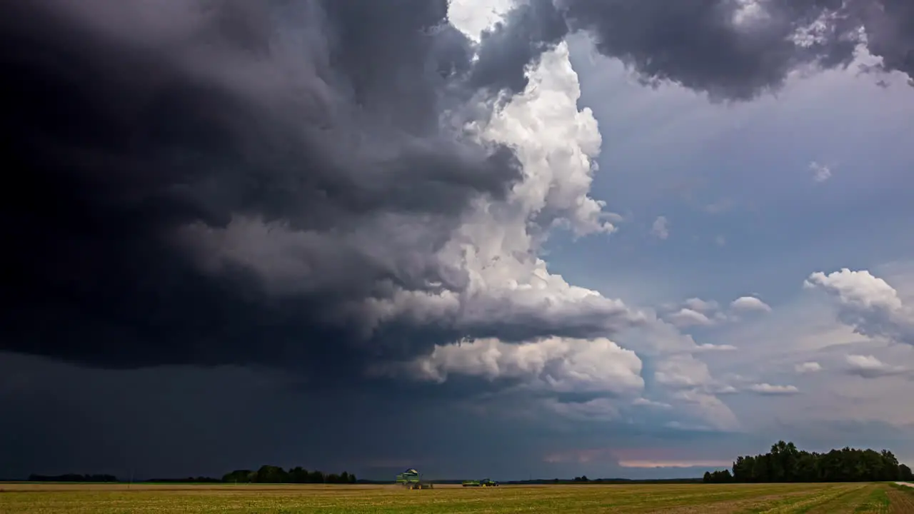 Shot of harvester moving along ripe wheat field with dark rain clouds passing by on a rainy day