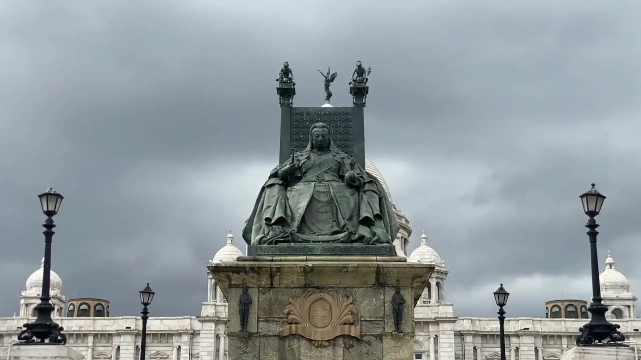 Low angle shot of statue of Queen Victoria sitting in front of Victoria Memorial in Kolkata India with dark clouds passing by