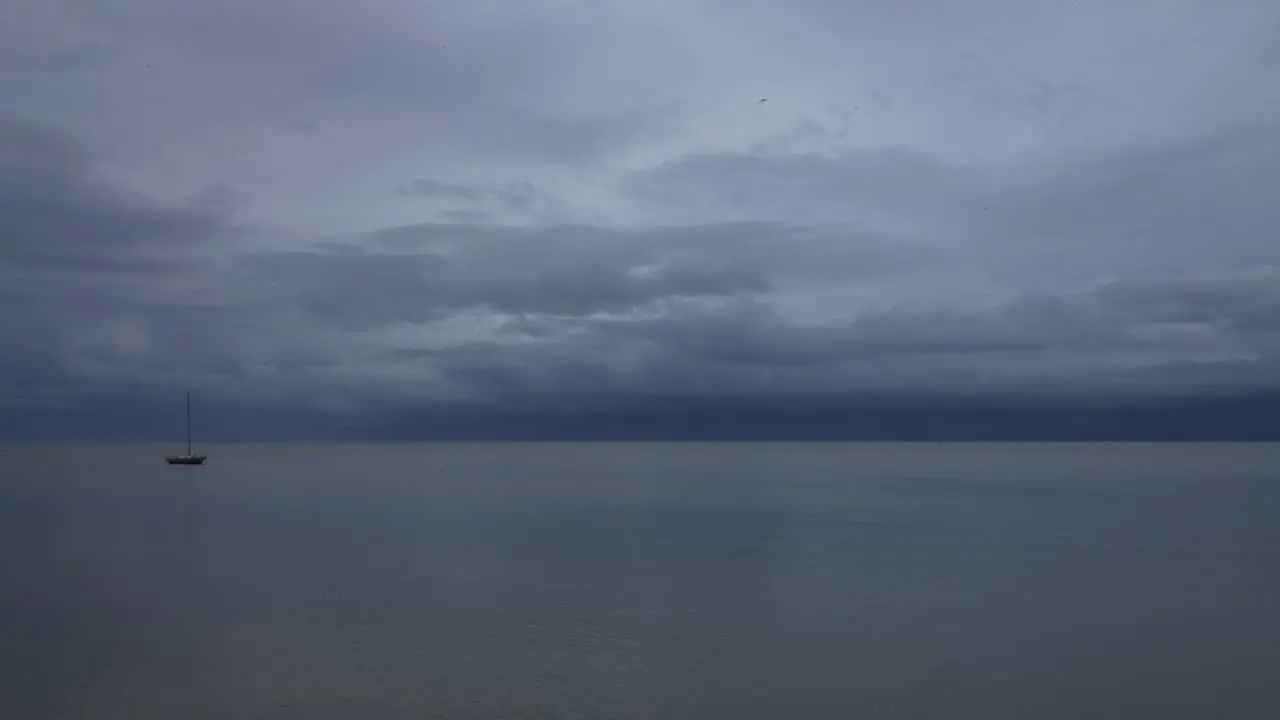 A lonely sailboat floating on the calm and glassy waters of a very cloudy day