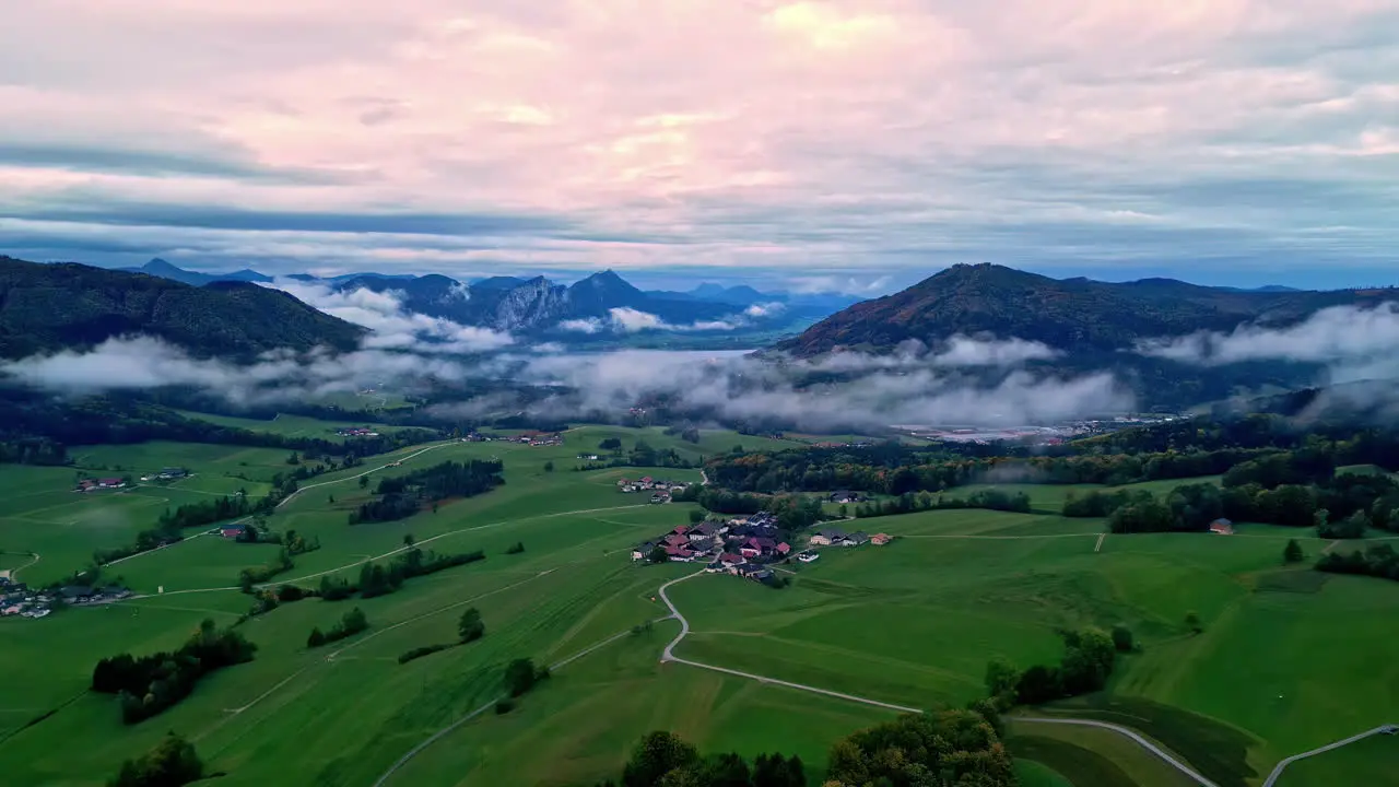 Aerial capture of a green landscape with few cluster settlements in the valley near high mountain summits under cloudy sky