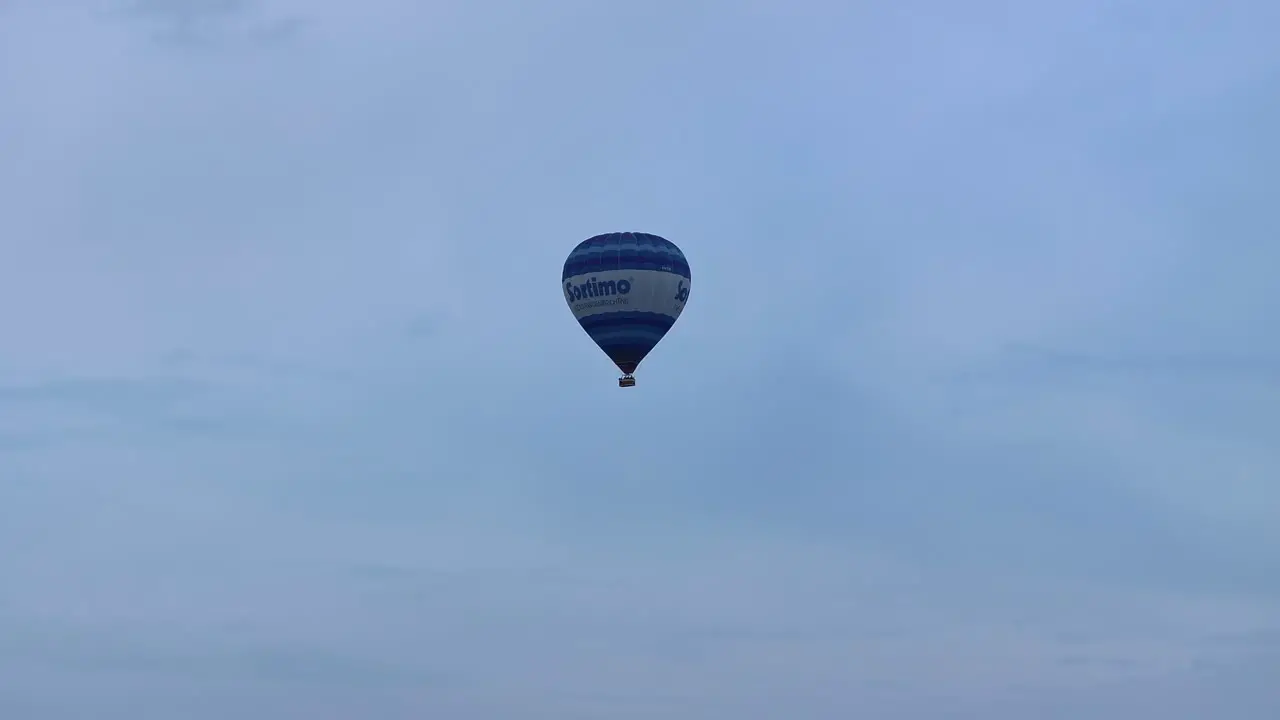 A blue hot air balloon floating skyward in a cloudy sky