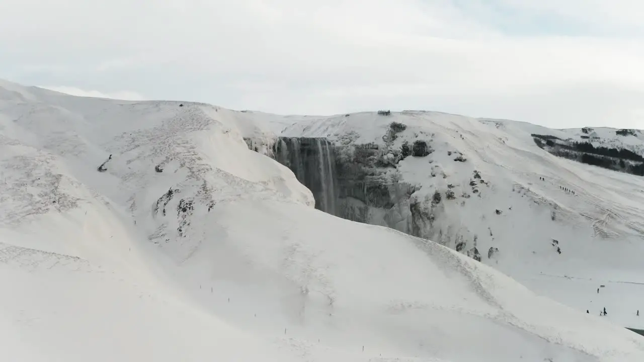 A beautiful large waterfall in Iceland in mid-winter covered by the snow around it and the clouds makes it even better