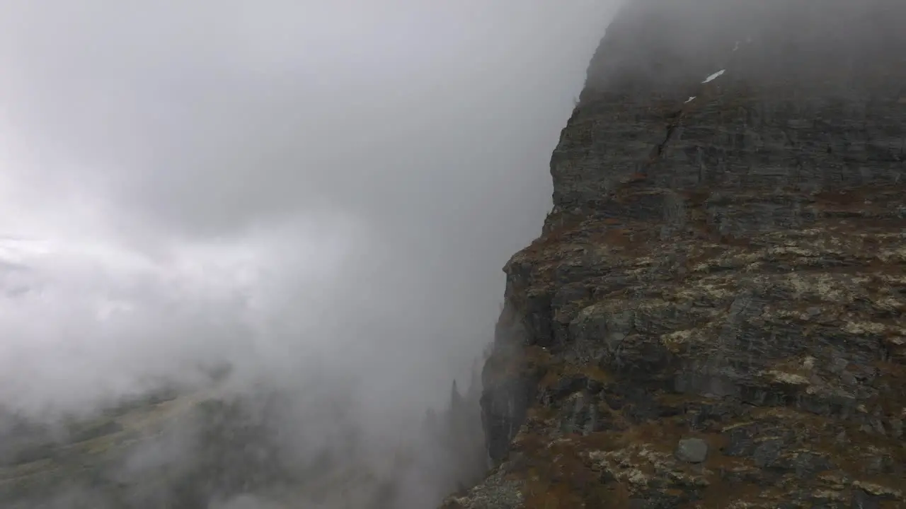 Big mountain wall with clouds surrounding it drone flying in to the clouds