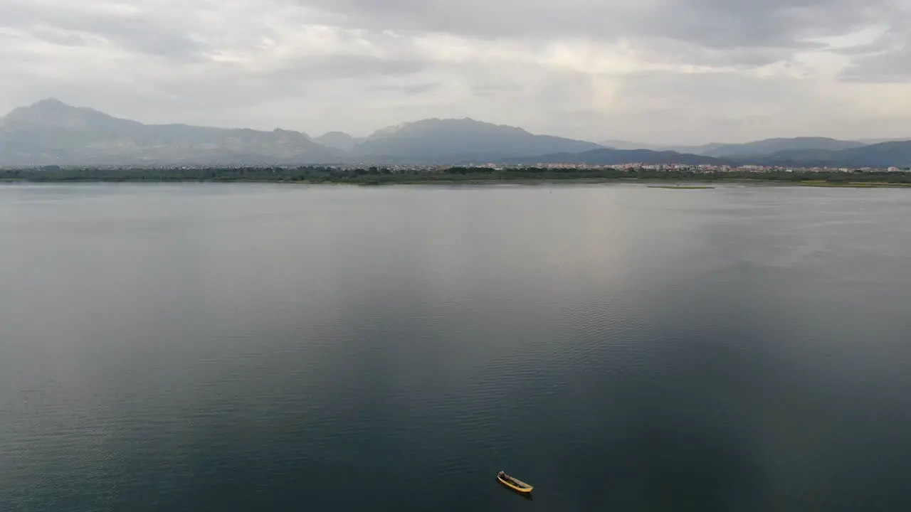 Drone view in Albania flying over Shkodër lake in Pogradec on cloudy day with mountains in the horizon and a yellow boat in the middle