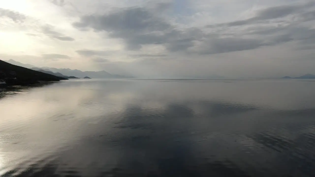 Drone view in Albania flying over Shkodër lake in Pogradec on cloudy day with shadowy mountains in the horizon