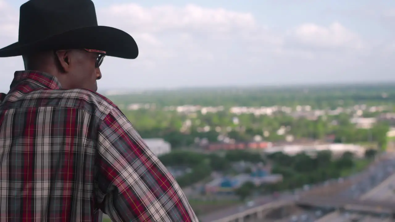 Black man with cowboy hat looking out over balcony