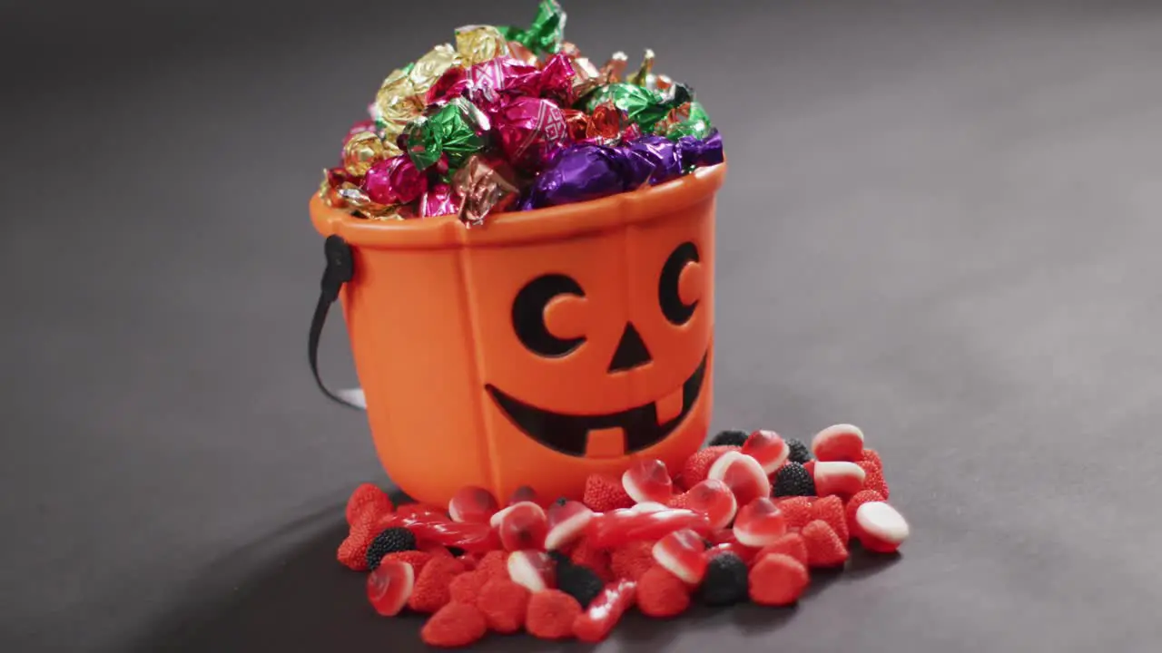 Scary halloween pumpkin printed bucket full of candies against grey background