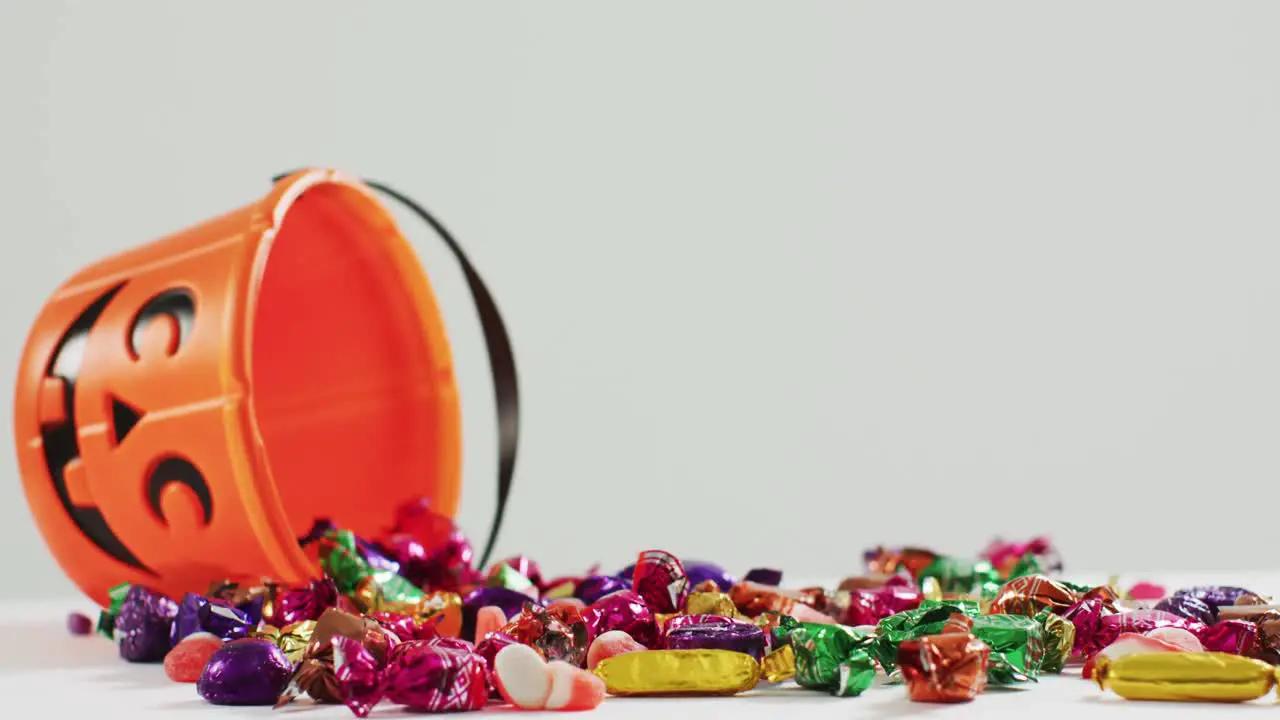 Scary halloween pumpkin printed bucket full of candies fallen against grey background