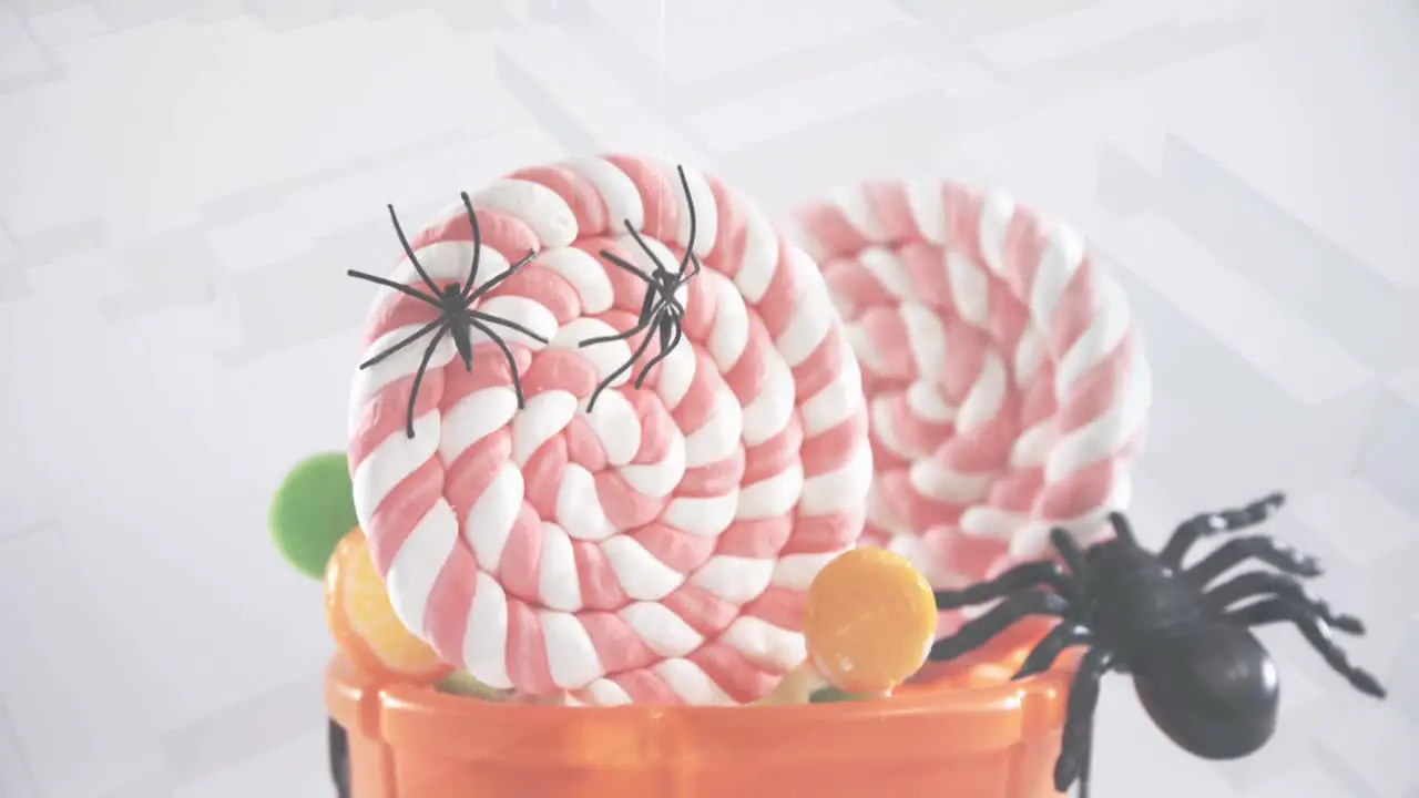 Spiders falling over in halloween pumpkin bucket filled with candies against 3d concentric shapes