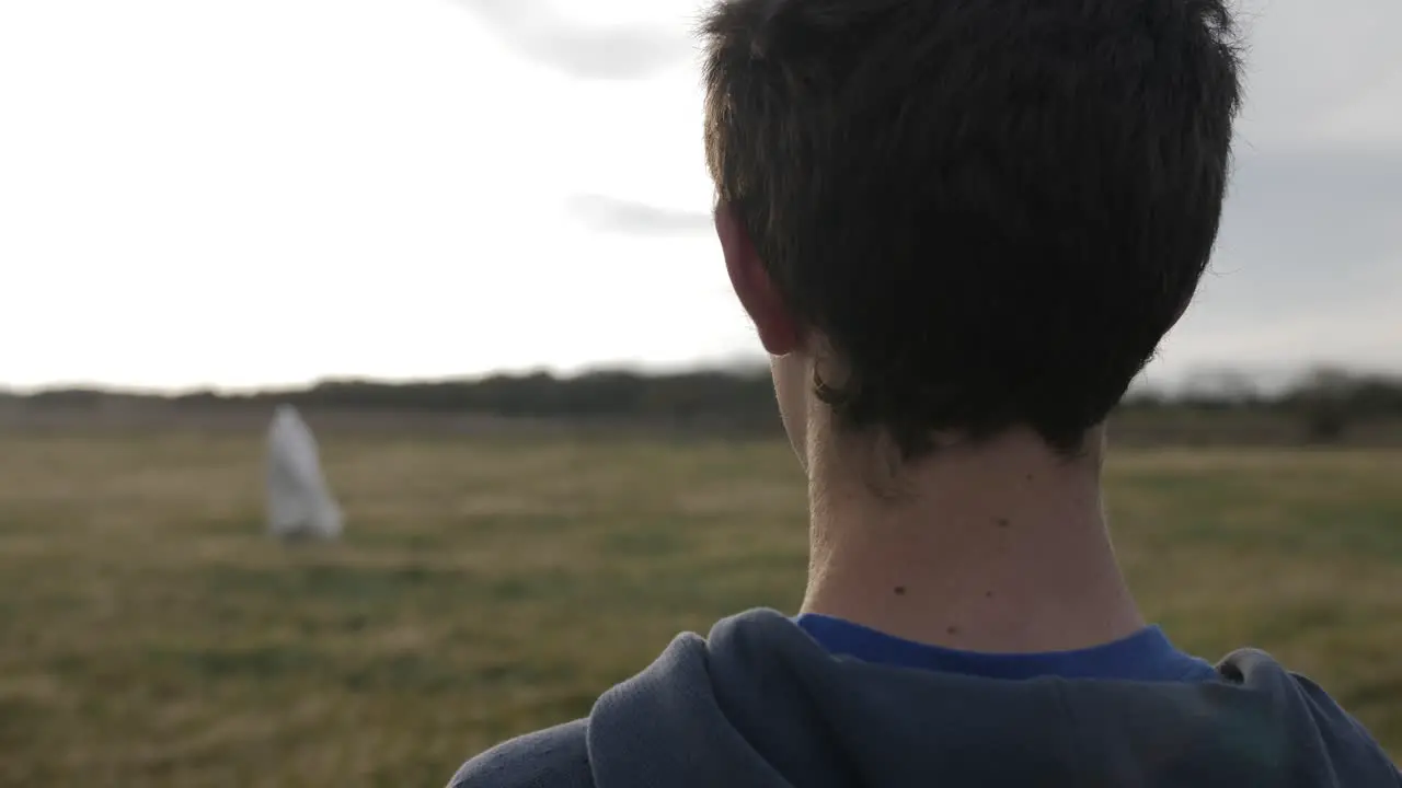 Teen boy looks at Jesus or a man wearing a white robe standing in the distance with light shining from the sun