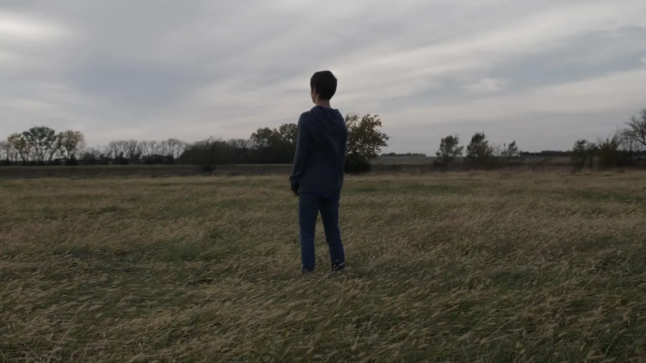 A teen boy stands in a Kansas field by himself watching the sun setting