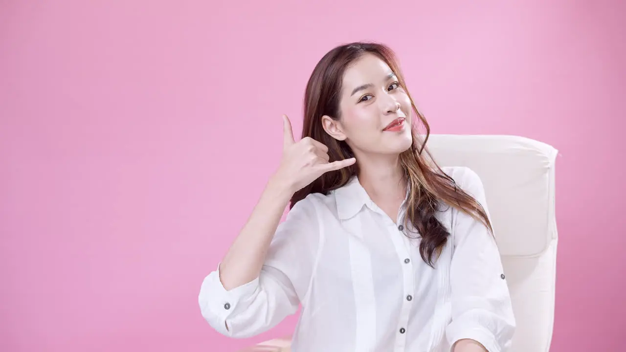 Young Asian woman making phone call motion with hands in the studio with pink background