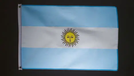 Studio Shot Of Flag Of Argentina Falling Down Against Black Background