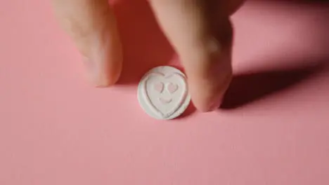 Hand Picking Up Heart Candy With Love Emoji On Pink Background