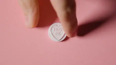 Hand Picking Up Heart Candy With Hug Me Message On Pink Background