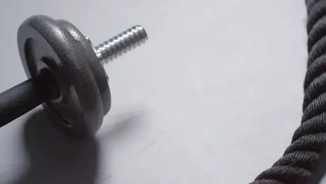 Close Up Studio Fitness Shot Of Hand Picking Up Gym Weight On Grey Background With Battle Rope