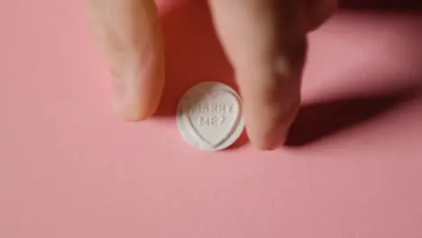 Hand Picking Up Heart Candy With Marry Me Message On Pink Background