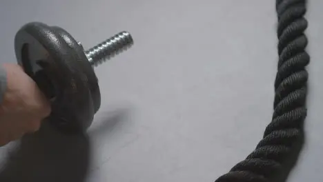 Close Up Studio Fitness Shot Of Hand Putting Down Gym Weight On Grey Background With Battle Rope