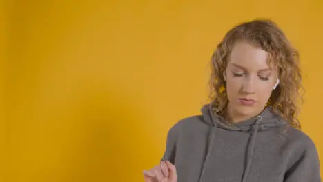 Studio Shot Of Young Woman Listening To Music On Mobile Phone And Dancing Against Yellow Background