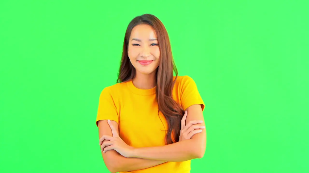 A pretty young woman against a green background smiles as she crosses her arm in front of her